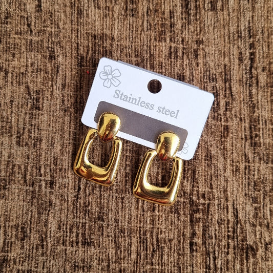 Gold earrings on a brown textured surface with a visible brand tag.