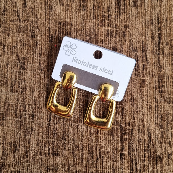 Gold earrings on a brown textured surface with a visible brand tag.