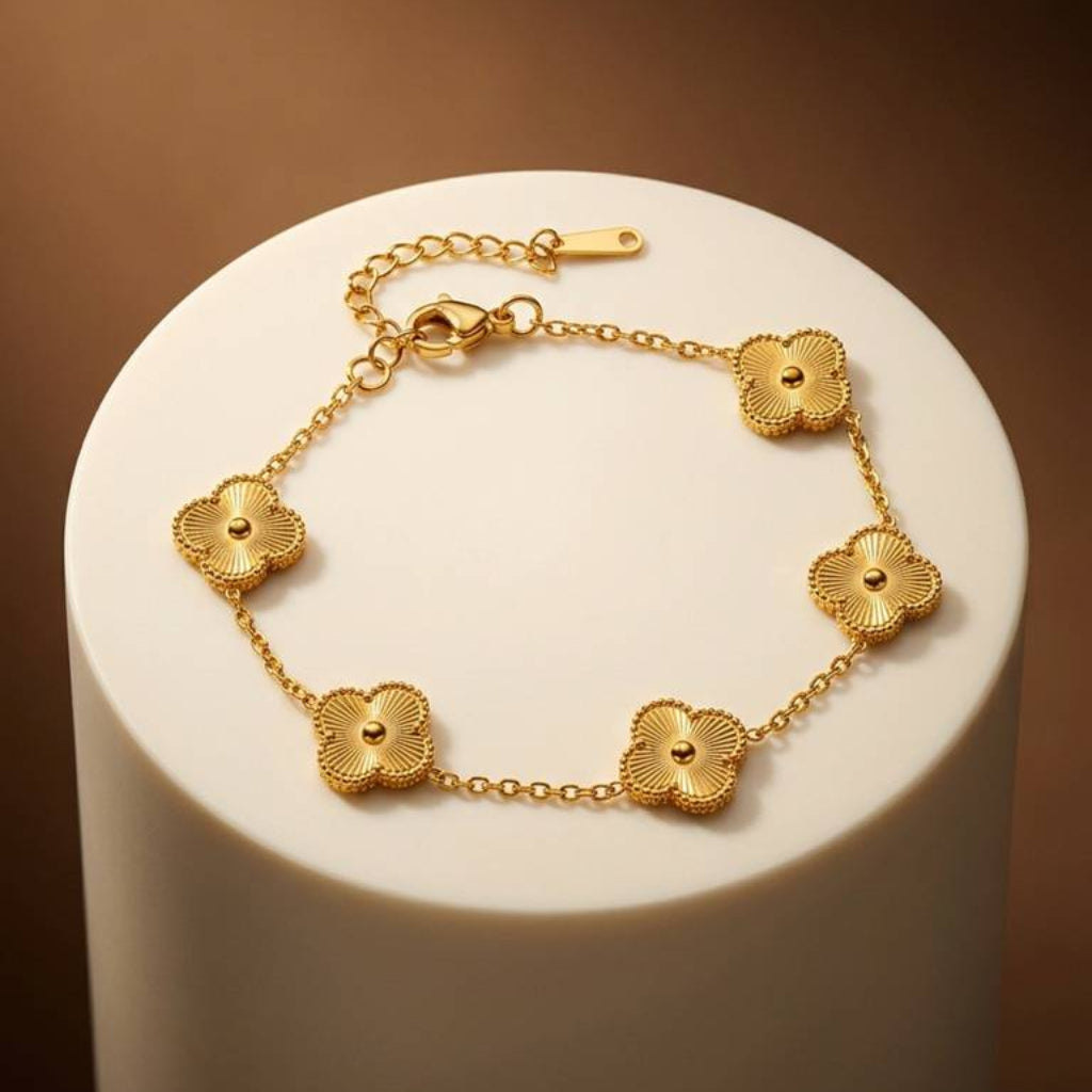 A gold chain bracelet with five textured, flower-like oval links, displayed on a white cylindrical pedestal against a warm brown background.