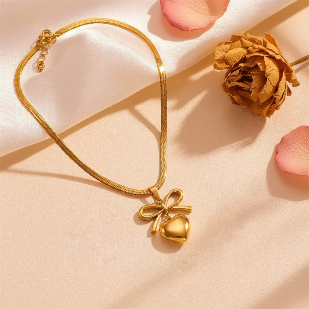 Gold bow heart pendant necklace flat lay on blush satin with dried flowers